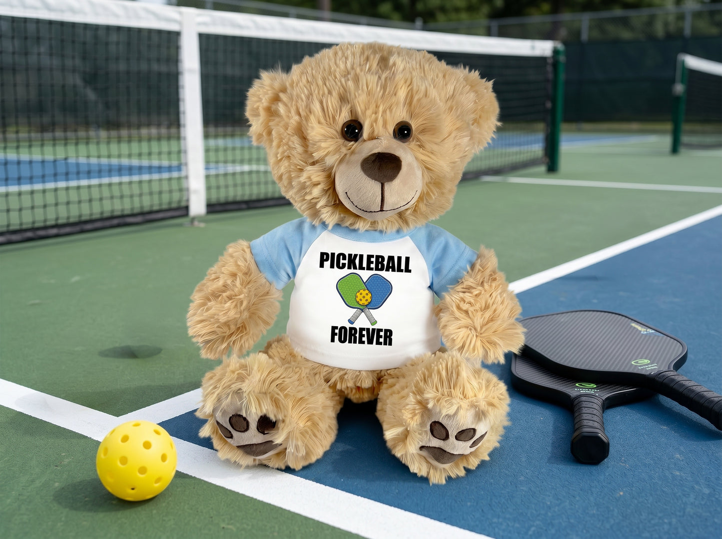 Personalized Pickleball Teddy Bear - 14" Honey Bear, Paddle Design- light blue sleeve shirt, pictured on pickleball court. Perfect gift for pickleball players.